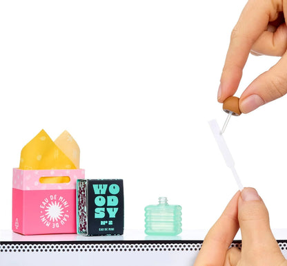 Hands placing a mini fragrance tool beside a pink box and teal mini bottle