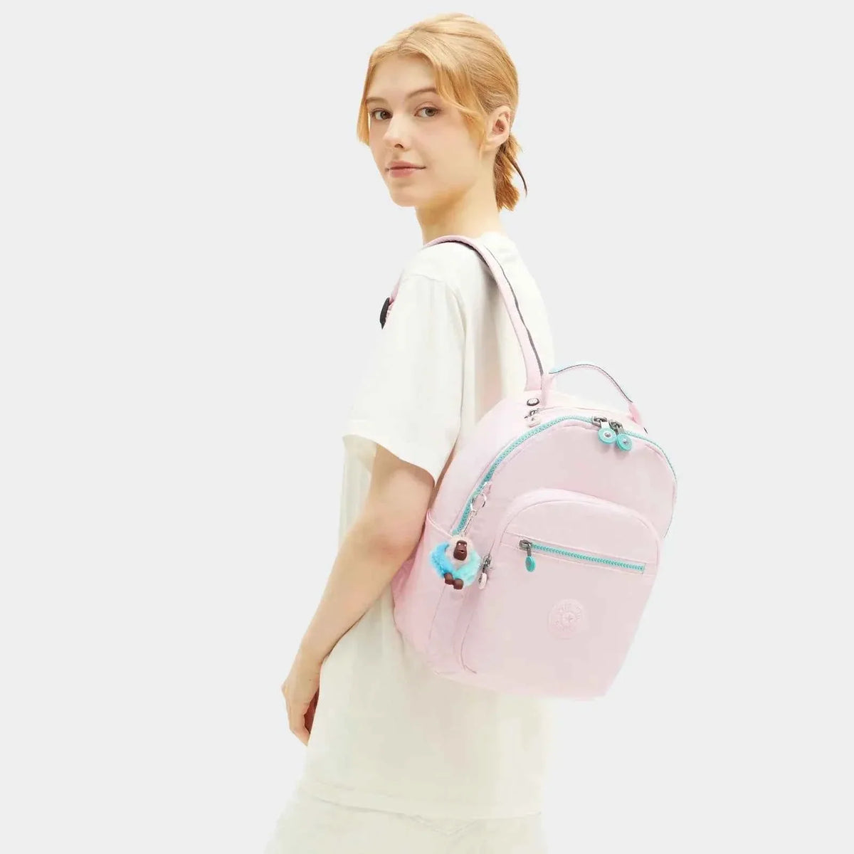 Seoul S mini backpack on model, pale pink with teal accents and plush keychain