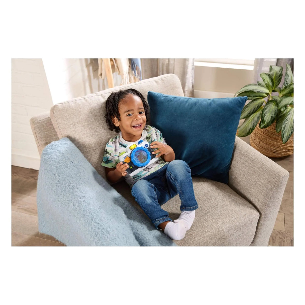 Child holding a blue VTech snap-and-smile camera while sitting on a couch