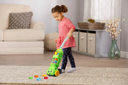 Green vacuum toy with smiling face and colorful parts, with small counting pieces on floor
