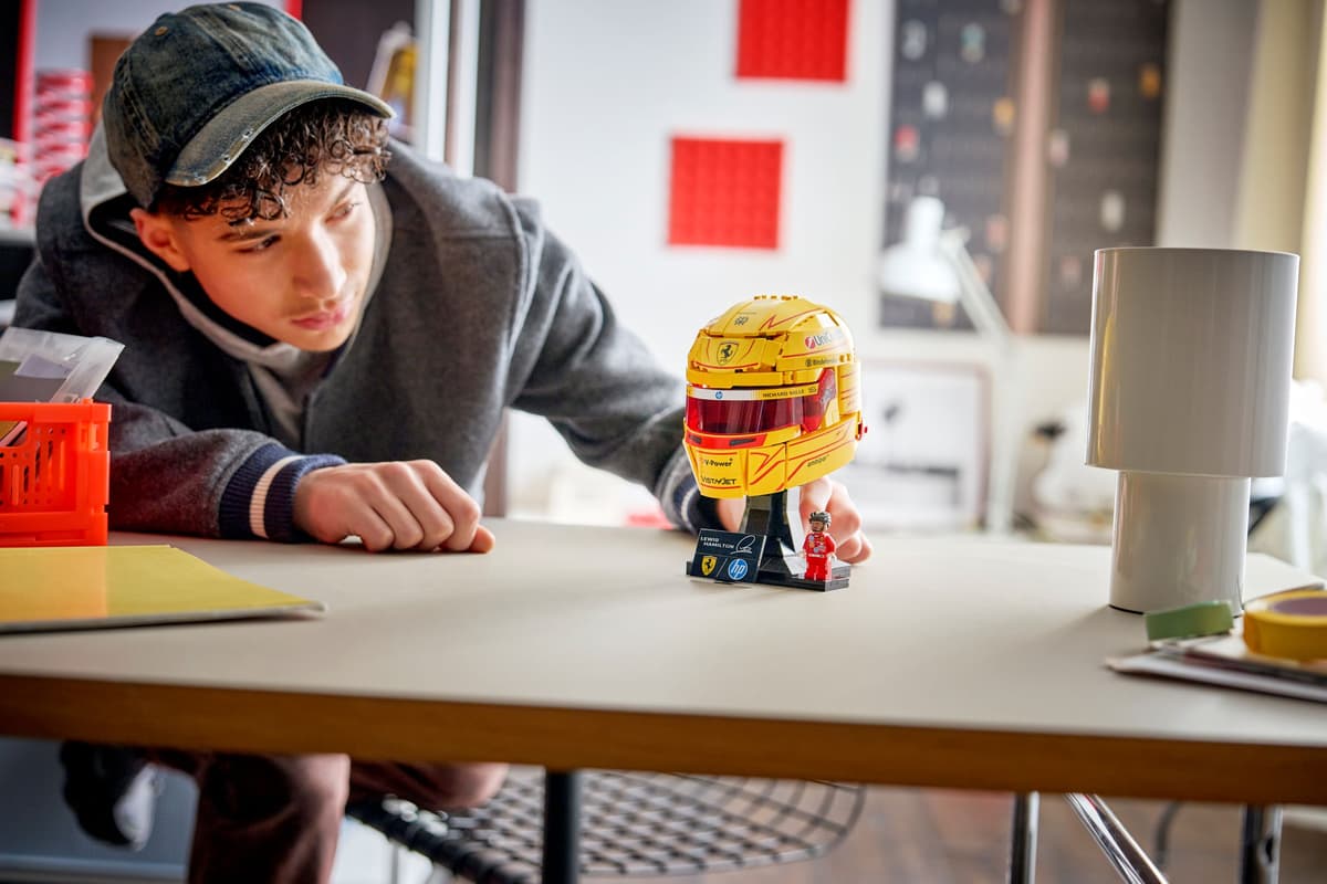 Yellow racing helmet model on black stand near small figure on desk