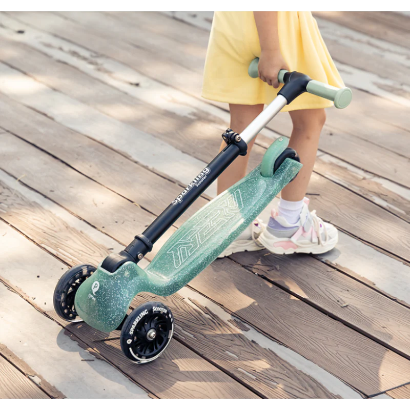 Green sparkling kids scooter with three wheels and mint handlebar grips on wood
