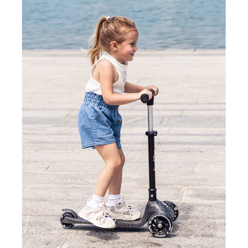 Black sparkling kids scooter with handlebar and three wheels, ridden by a child
