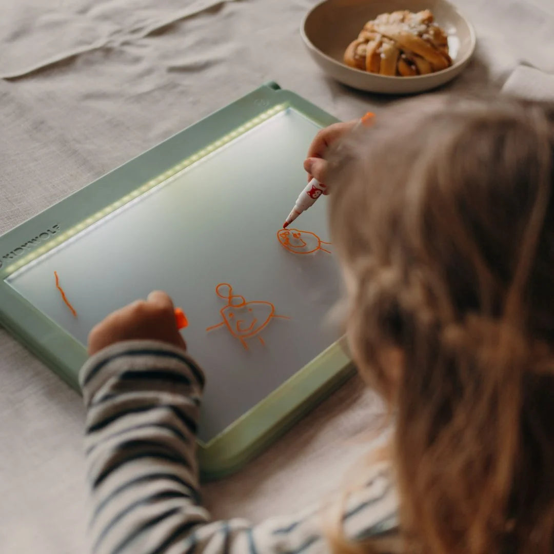 Kids marker set: child draws orange doodles on a green light board