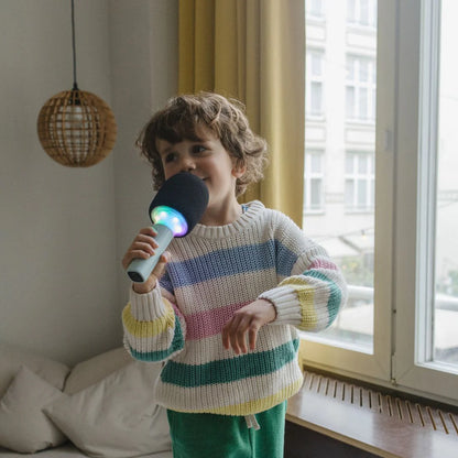 Kid holding Kidymic karaoke microphone with dark foam head and mint handle, glowing