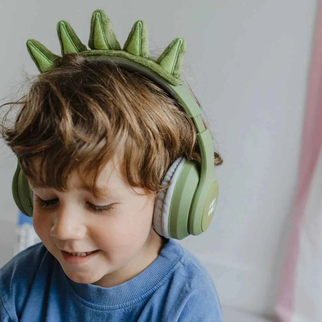 Child wearing green dinosaur-style Bluetooth headphones with gray ear pads
