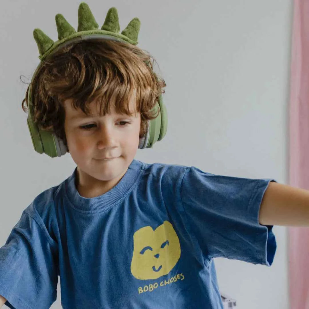 Child wearing green dinosaur Bluetooth headphones and blue graphic shirt