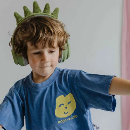Child wearing green dinosaur Bluetooth headphones and blue graphic shirt