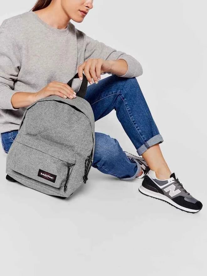 Light gray backpack held by a person, with front zip pocket and black logo patch