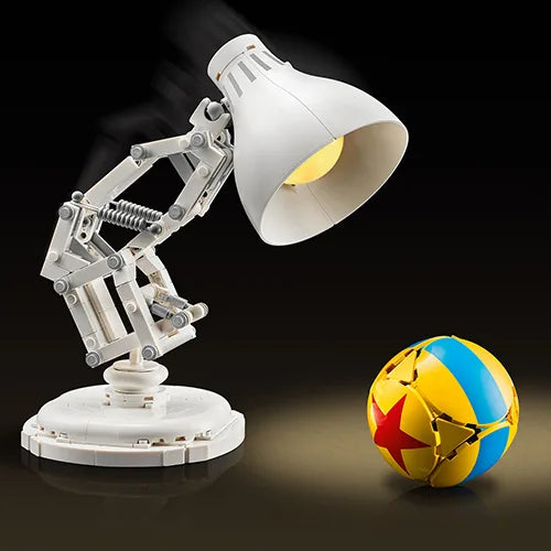 White articulated desk lamp with large shade and warm yellow bulb beside a globe ball