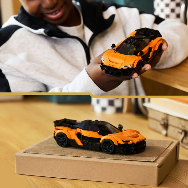 Orange toy sports car on a cardboard box, held in hand with black roof and wheels.