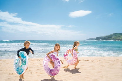 Inflatable pool tubes with tropical floral designs on beach, pink and blue rings