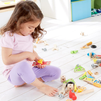 Child using wooden toy workbench with colorful pieces arranged on the floor