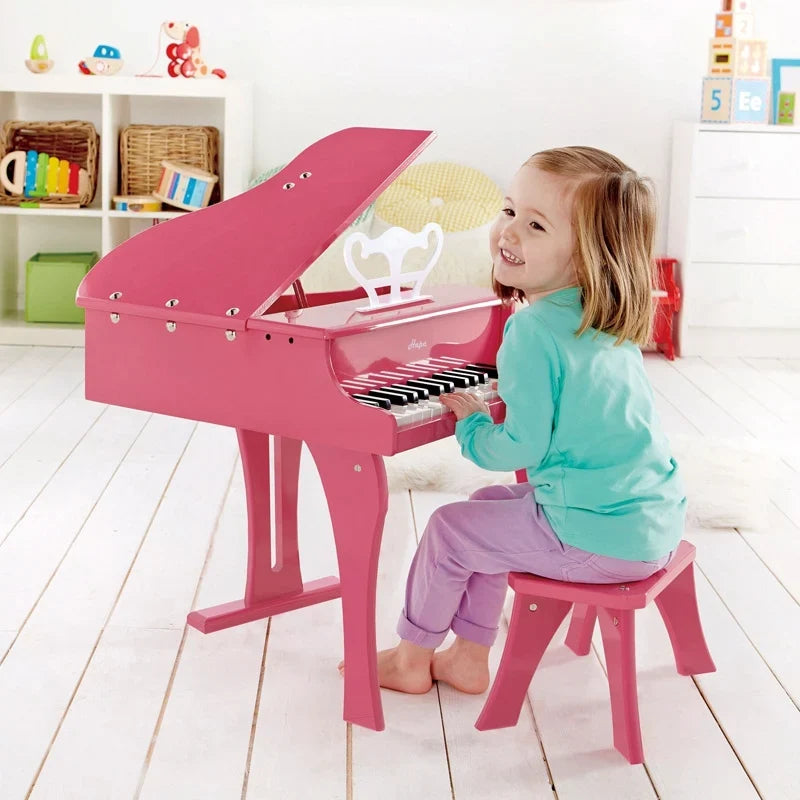 Pink toy grand piano with open lid and child playing on the bench