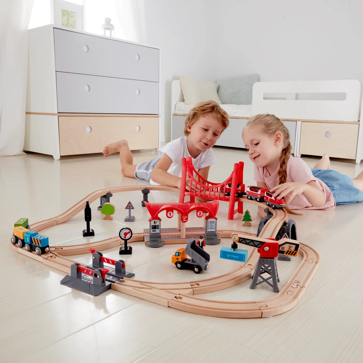Curved wooden railway with red overhead bridge, signals, trucks and toy trains