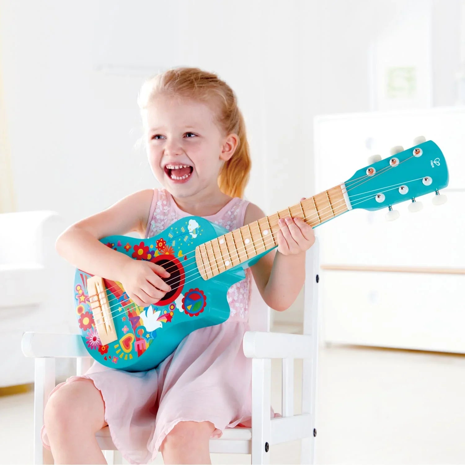 Turquoise toy guitar with rainbow flower and peace graphics, held by child