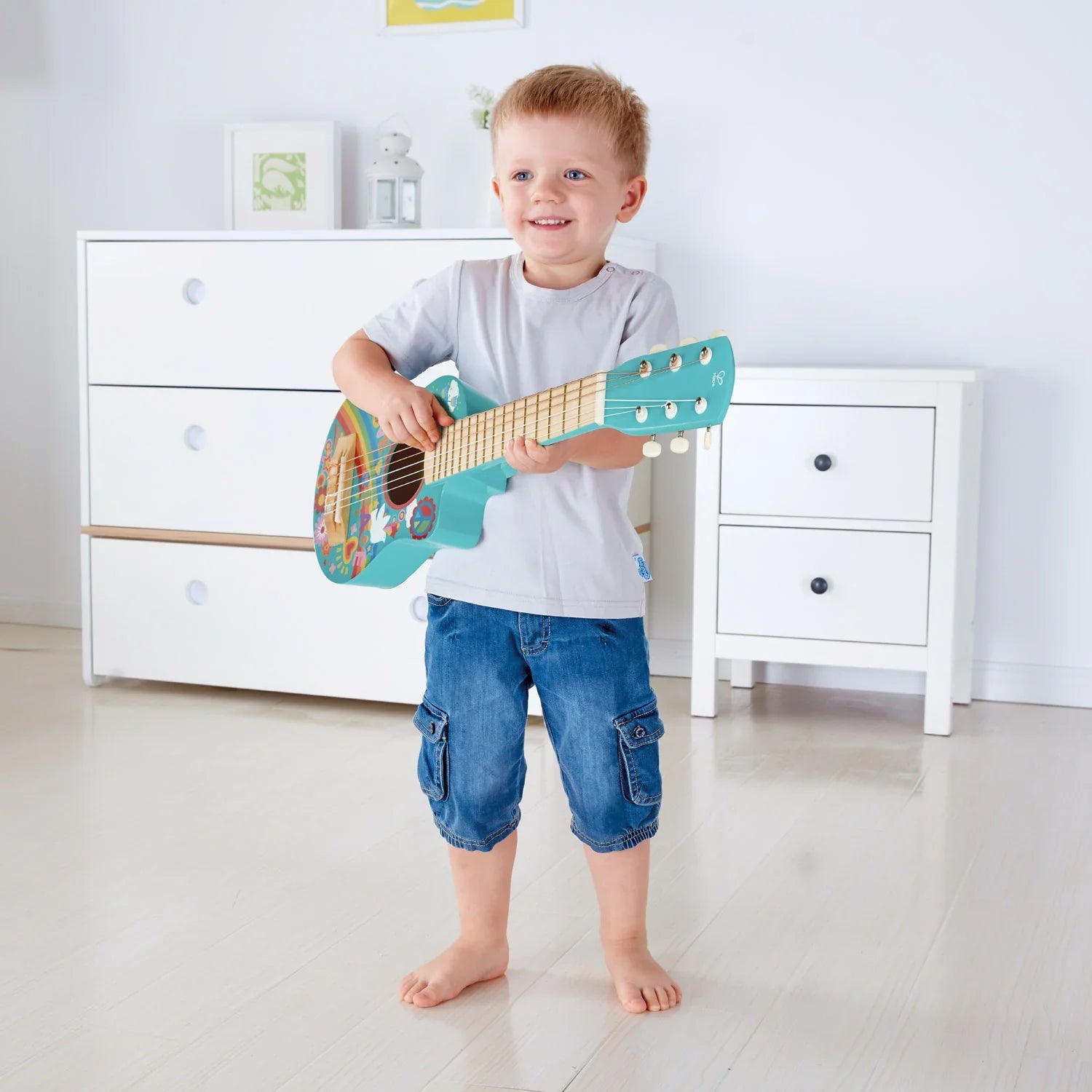 Turquoise kids toy guitar with teal headstock, tuning pegs, and colorful flower-power body