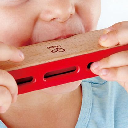 Wooden harmonica with red frame, held by a person near the mouth