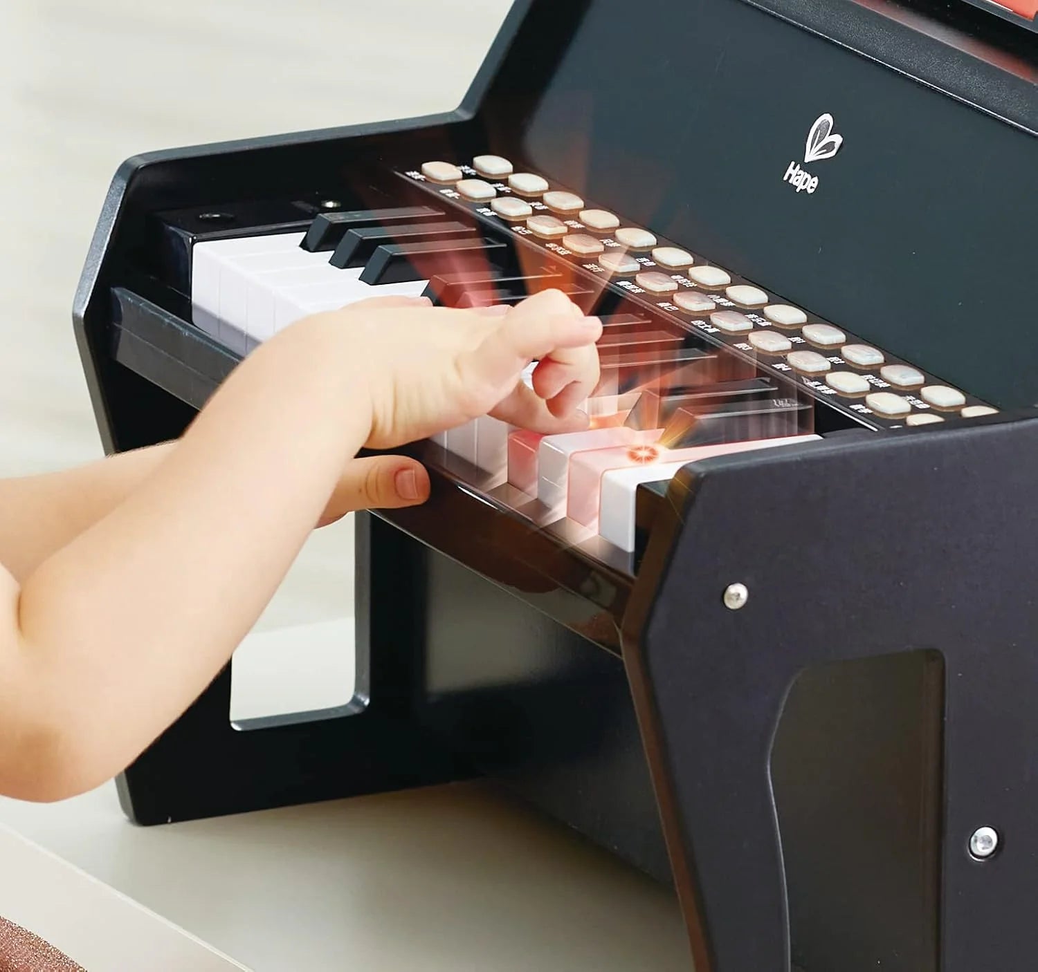 Hand pressing keys on black toy keyboard with white keys and color buttons