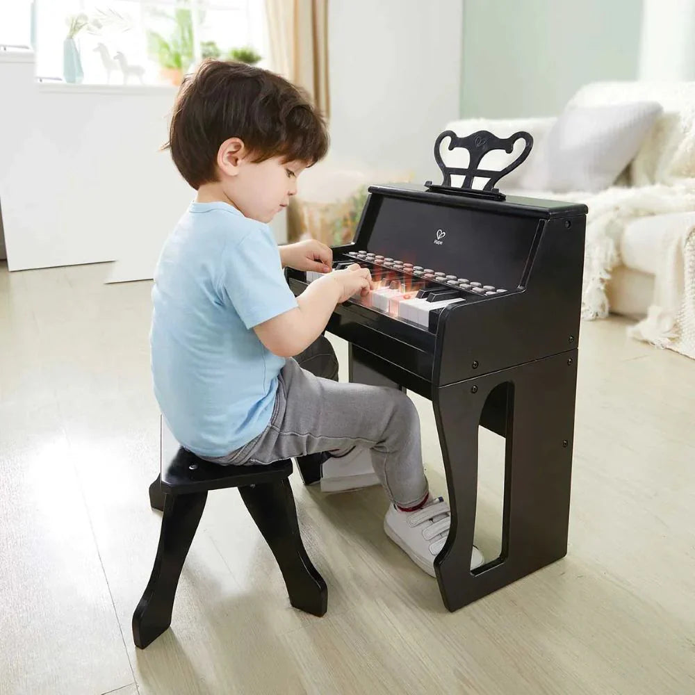 Schwarzes Kinderklavier mit geöffnetem Deckel, Kind sitzt am Hocker und spielt