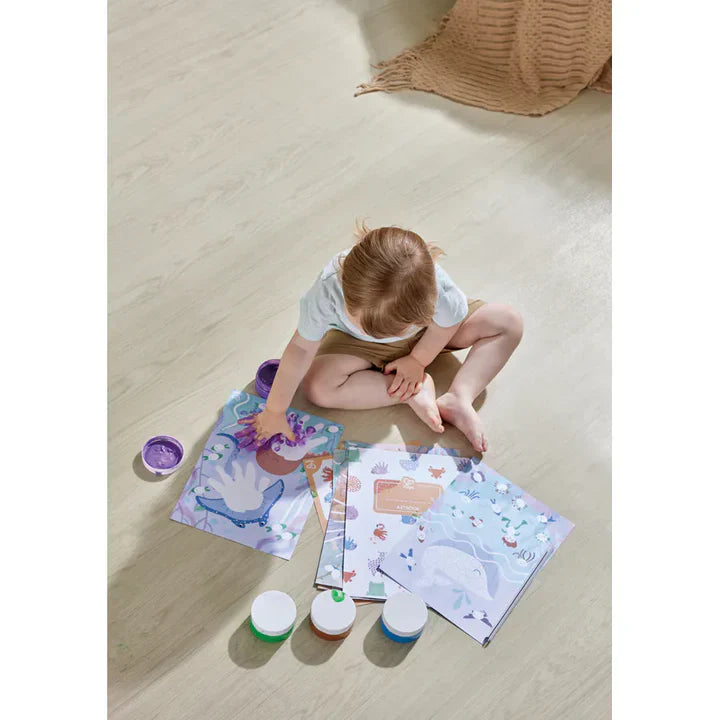 Child finger-painting with purple paint pots and dinosaur-themed activity sheets