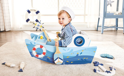 Blue rocking boat toy with sail, captain wheel and circular play panel, on floor