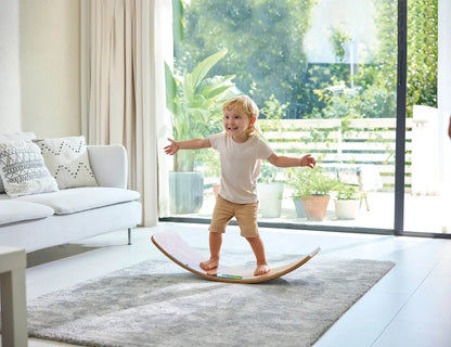 Balance board toy on carpet as child stands with arms out, lights visible on base
