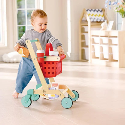 Toy shopping cart in red basket with teal wheels, child pushing on floor