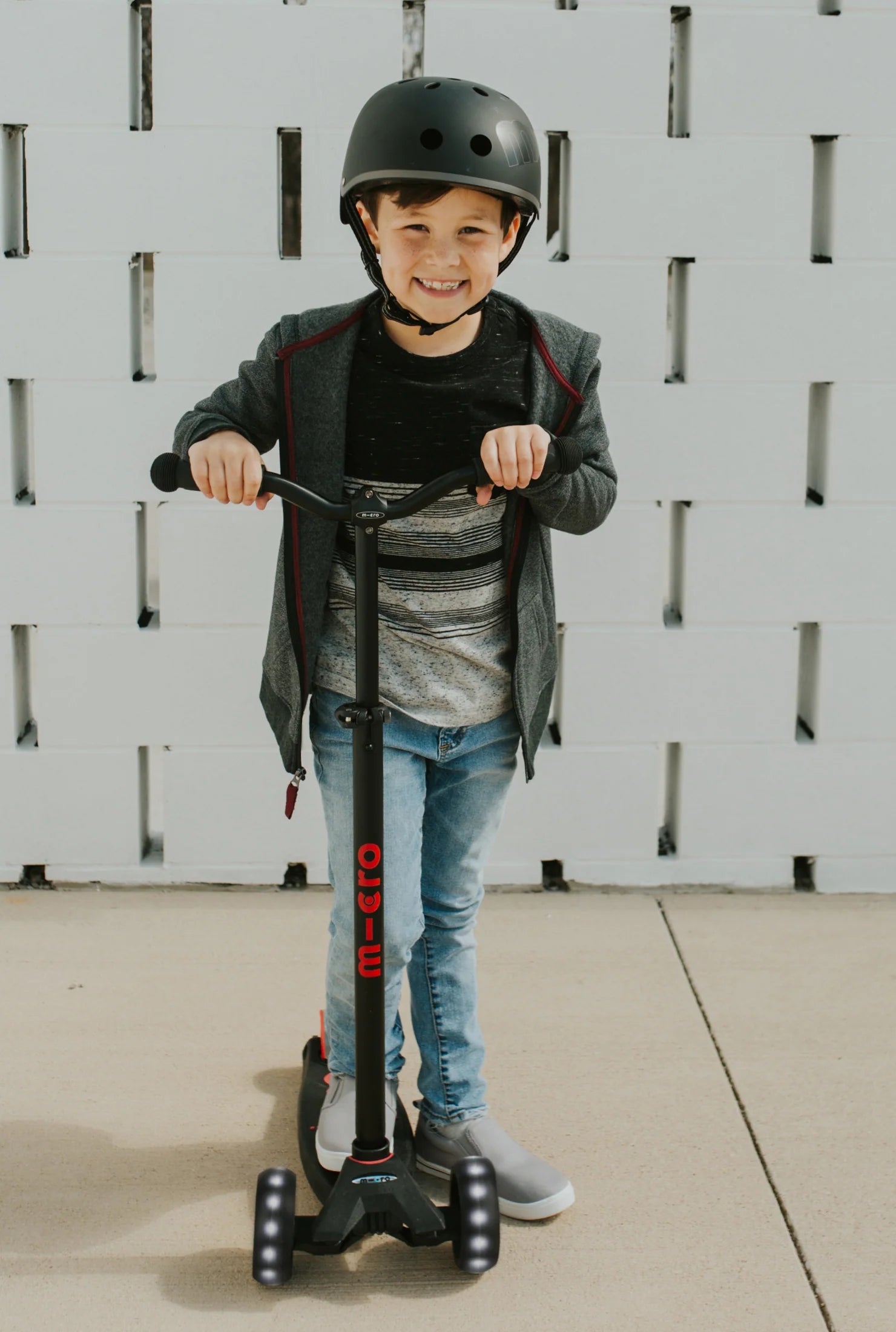 Child standing behind a dark LED scooter with handlebars and front wheels