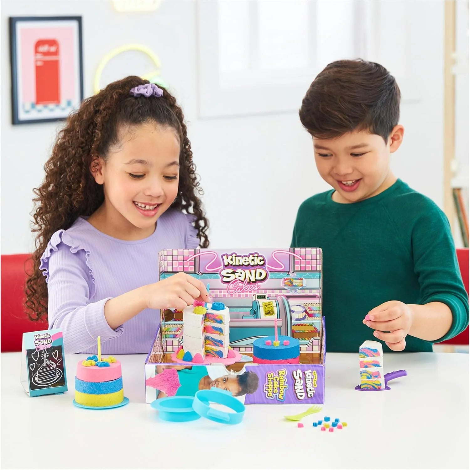 Kids playing with Kinetic Sand rainbow cake shoppe kit, tools, and tiered cake