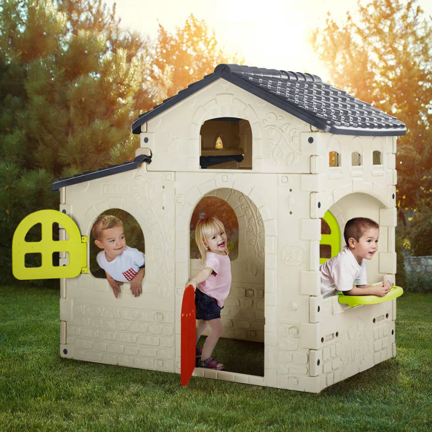 Large white playhouse with dark roof, arched windows, and green door panels outdoors