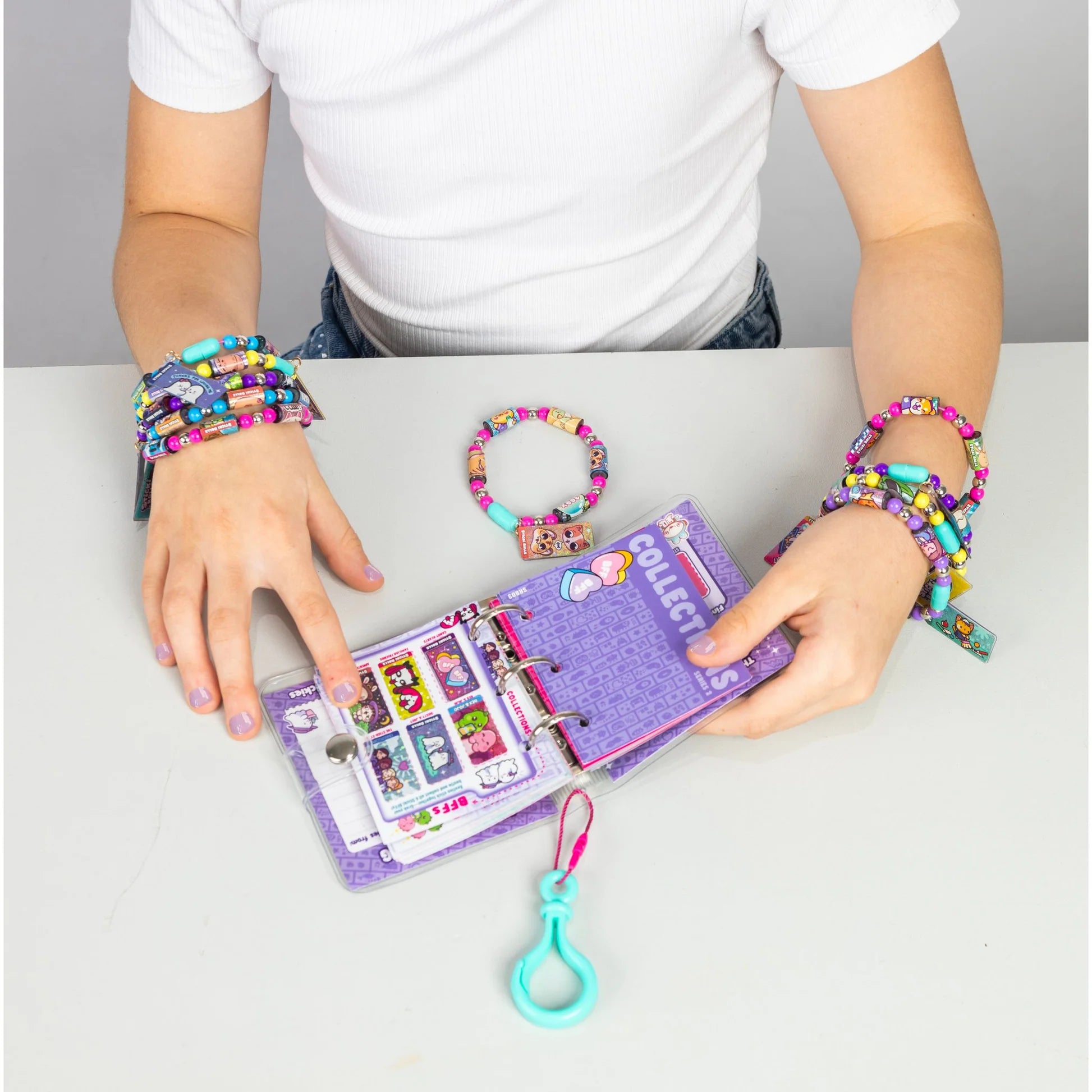 Hands wearing colorful beaded sticker bracelets with Sticki Book Series 2 open