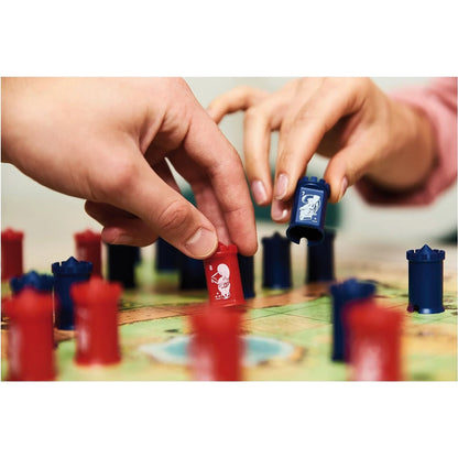 Hands placing blue and red board game pieces on a green game grid