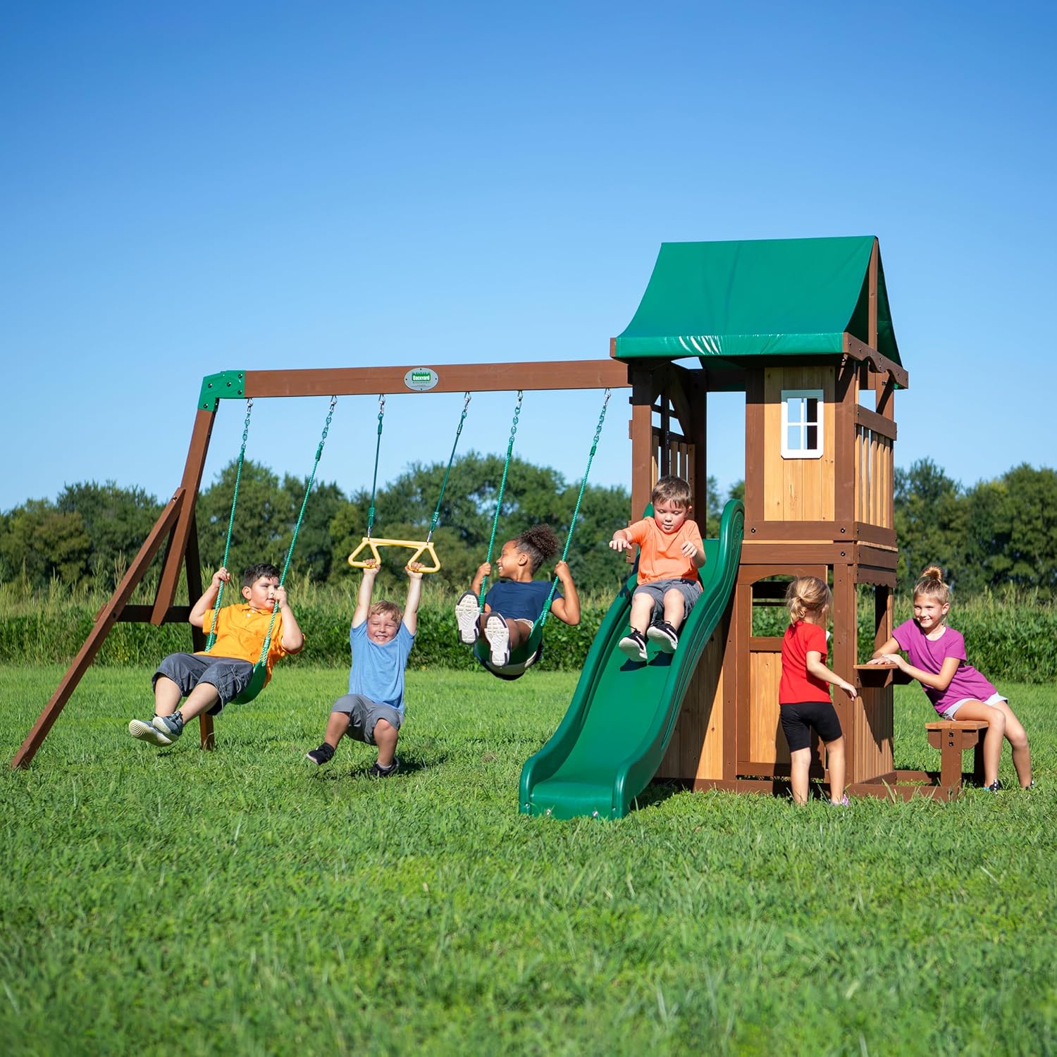 Wooden playset with swing seats and green slide next to playhouse tower