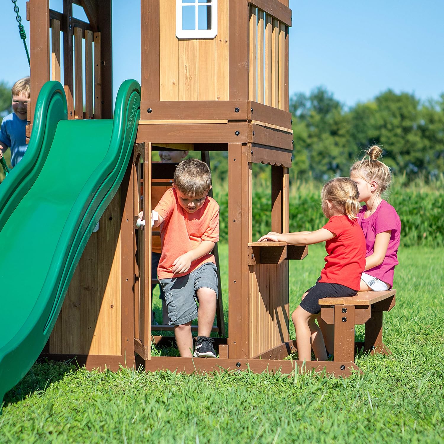 Green slide beside wooden playhouse with open window and front side doorway