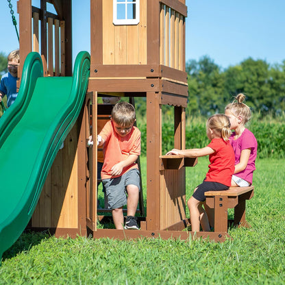 Green slide beside wooden playhouse with open window and front side doorway