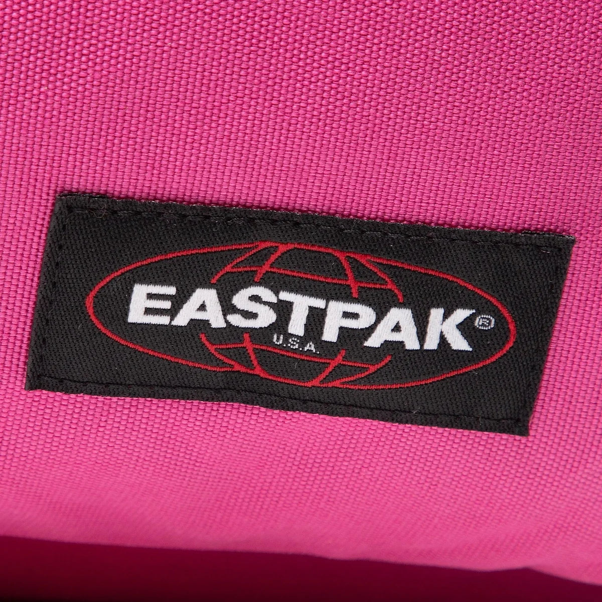 Pink backpack fabric with black Eastpak logo rectangular patch close-up