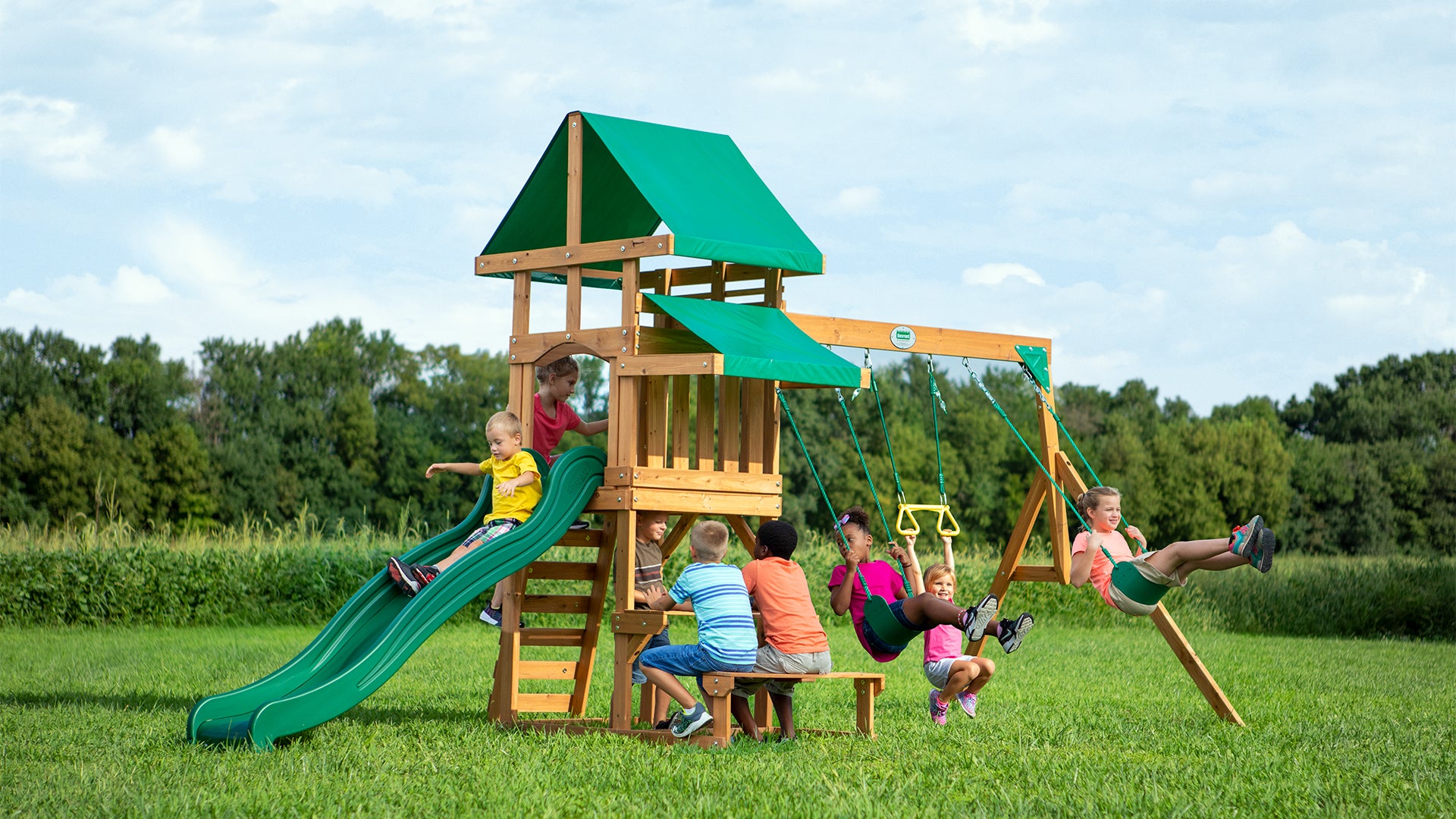 Angled view of cedar wood play tower with green slide and two rope swings