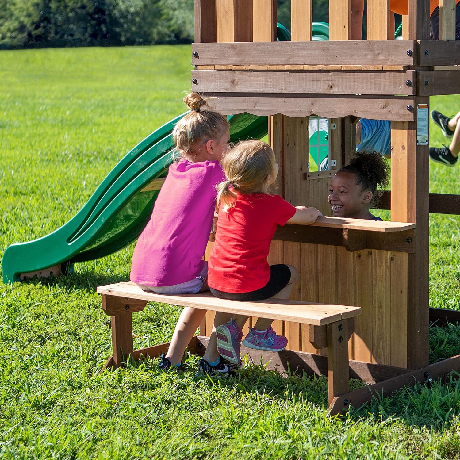 Green slide and covered playhouse bench area with open window on wooden wall