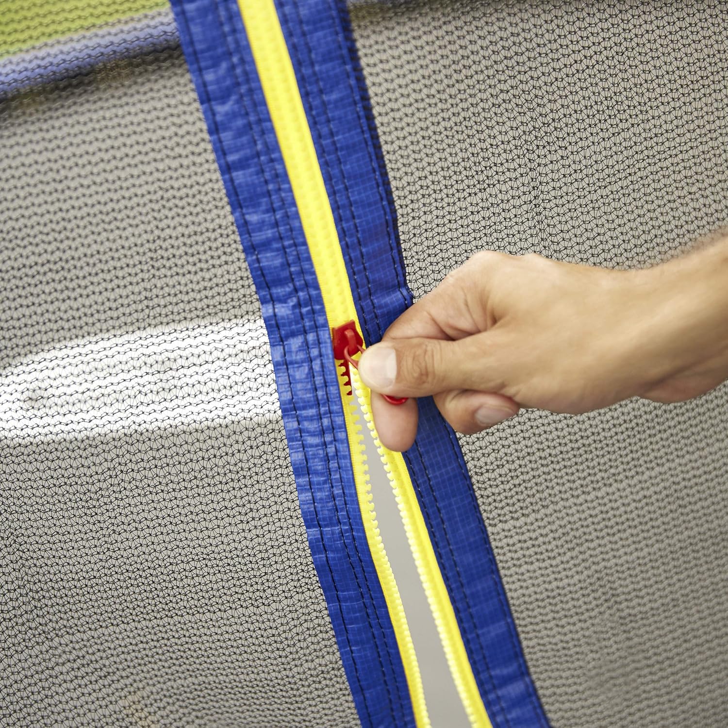 Trampoline safety net zipper seam, hand fastening a red latch on blue frame