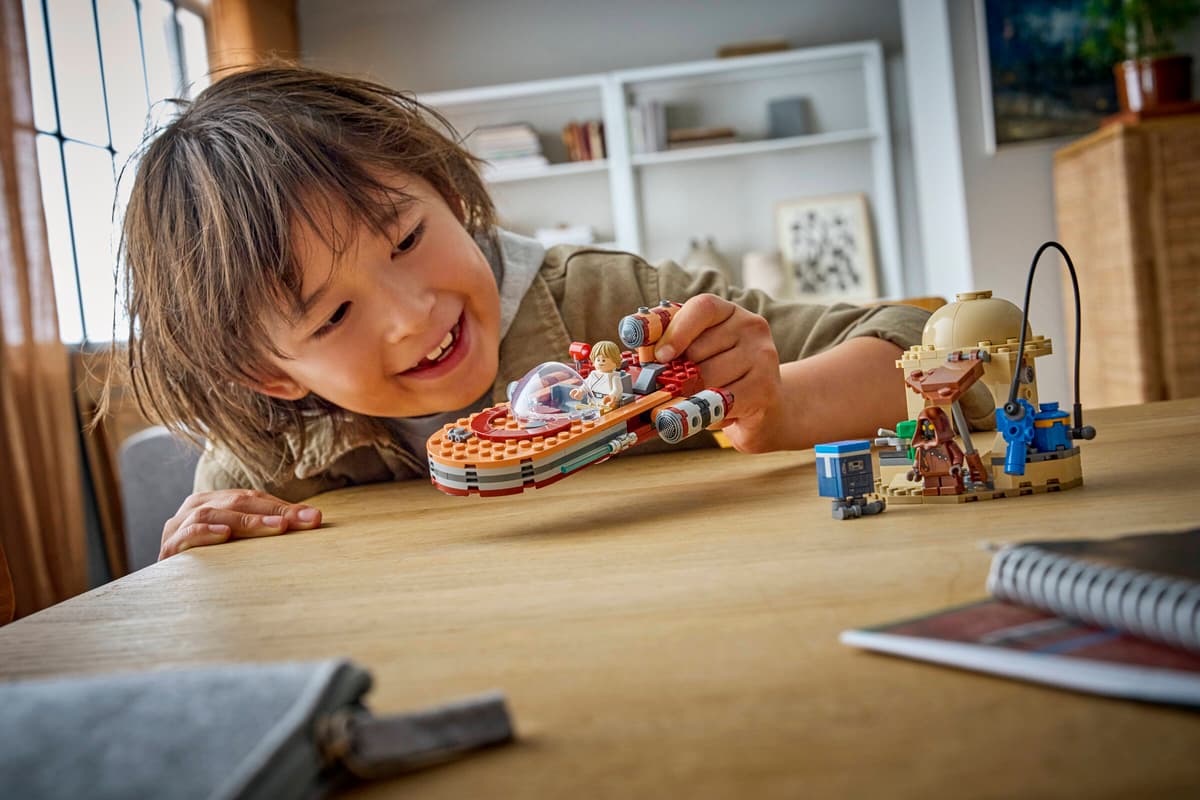 Child smiling while playing with Luke's Landspeeder LEGO set on table