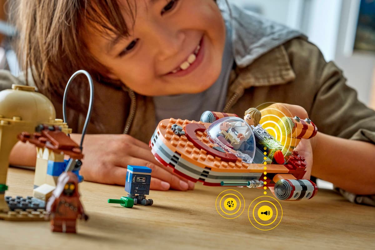 Child playing with Luke's Landspeeder LEGO model and Luke minifigure