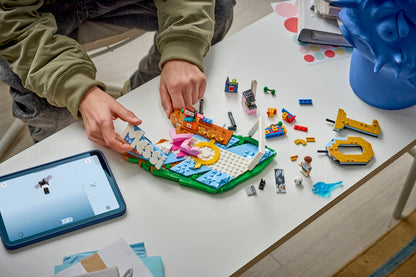Person building a LEGO soccer highlights model on a green baseplate with loose bricks