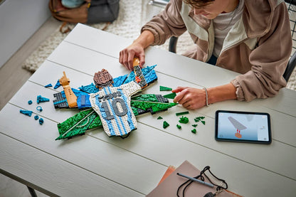 Person assembling the brick figure on a table with loose pieces and an open instruction page