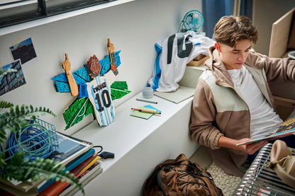 Brick-built Messi celebration figure on desk near tools, with person viewing the model
