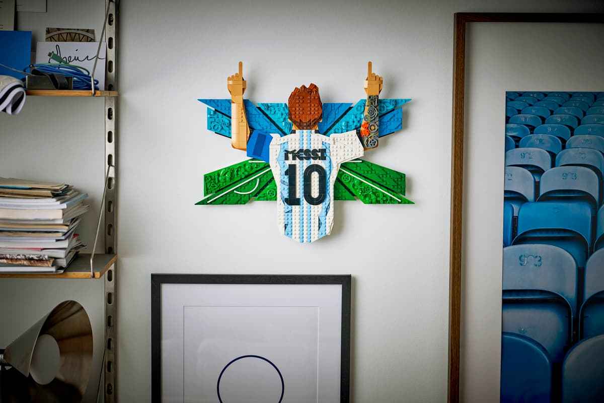 Brick-built Messi celebration figure displayed on wall above framed art
