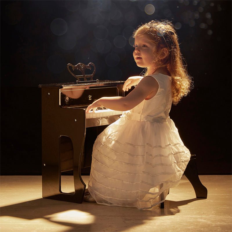 Black upright piano toy with child playing at the keyboard