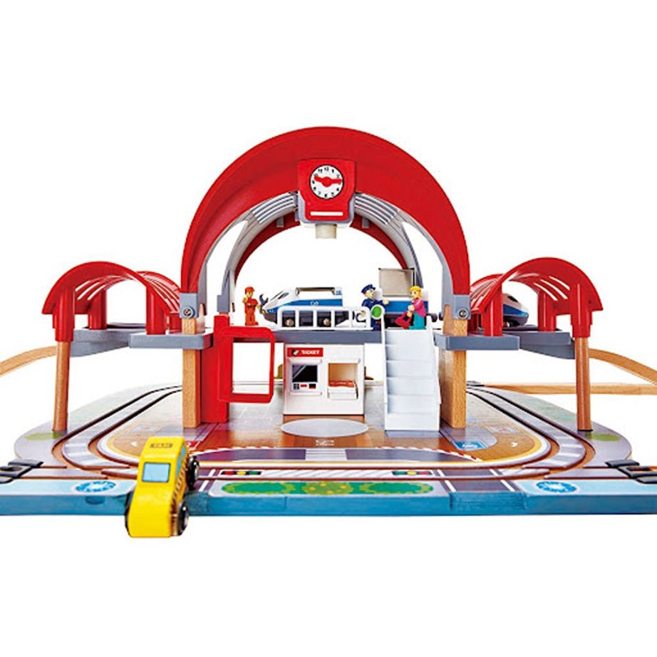 Toy train station playset with red arch, blue platform, tracks and small vehicles
