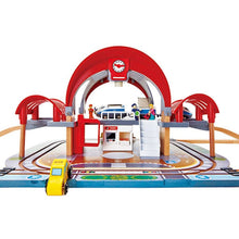 Toy train station playset with red arch, blue platform, tracks and small vehicles