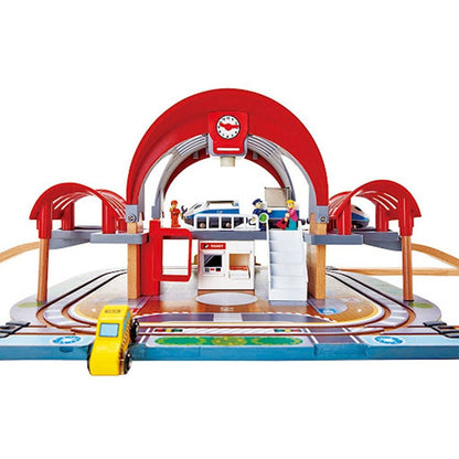 Toy train station playset with red arch, blue platform, tracks and small vehicles